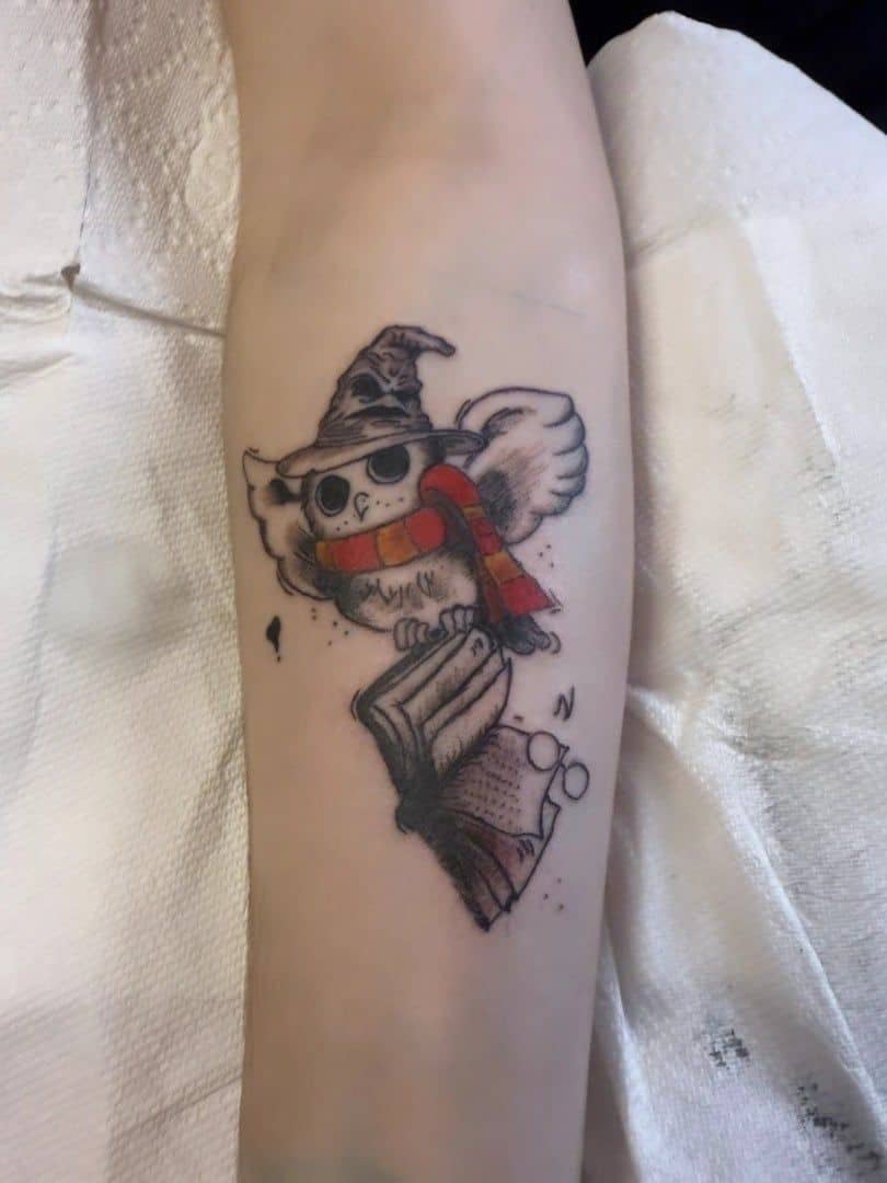 Tattoo by Jake Brewer, owl in a wizard hat and striped scarf on a forearm