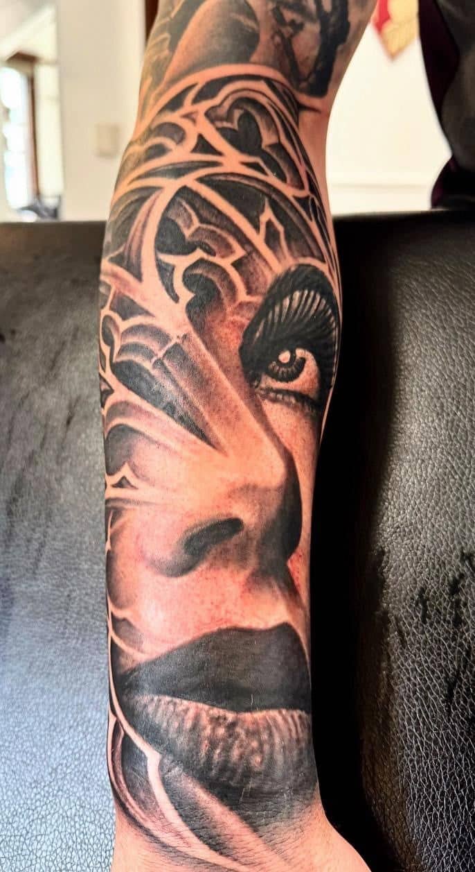Tattoo by Ricardo Mendes, woman's face in black and grey realism with filigree, on a forearm